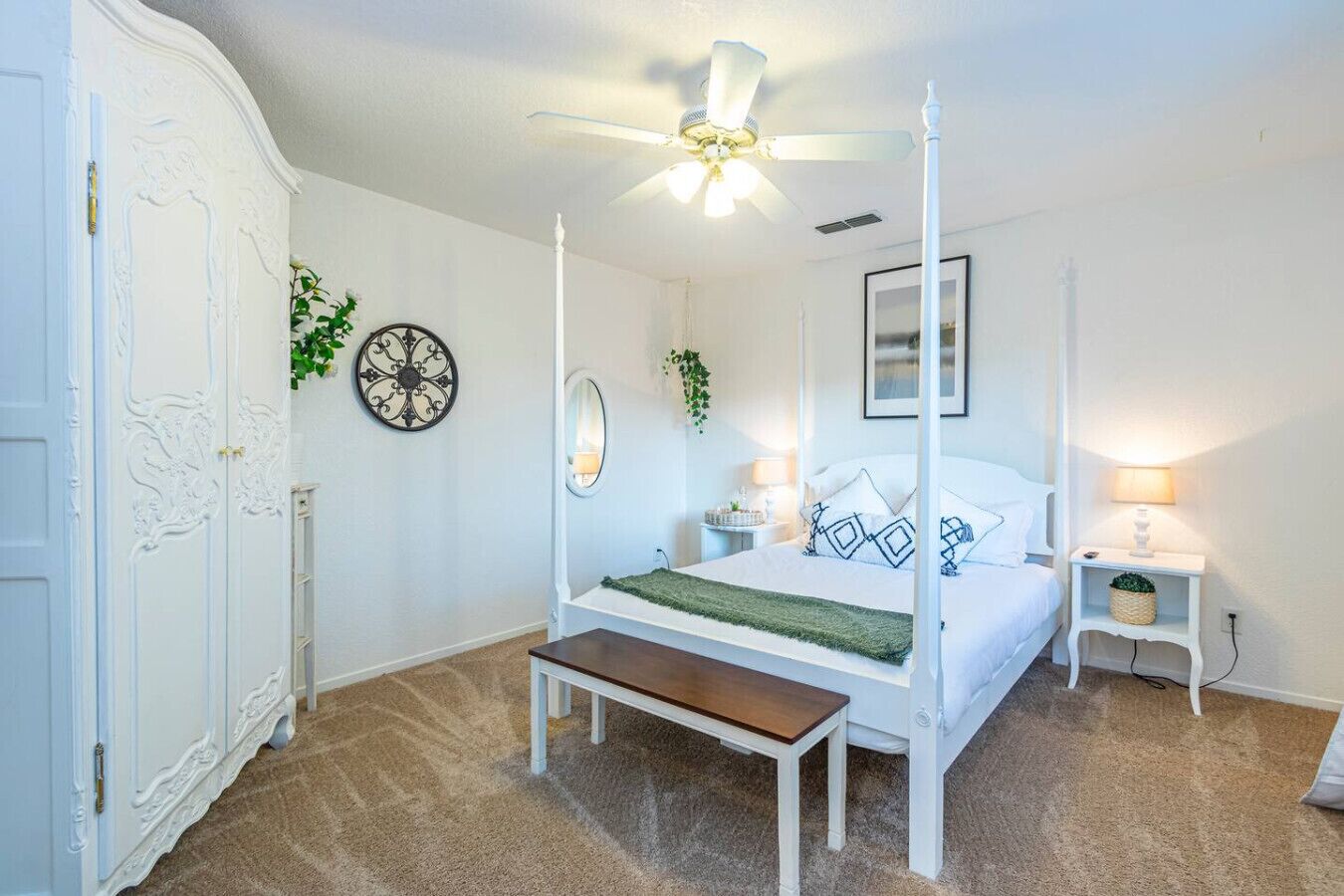 Una cama con dosel, mesitas de noche con lámparas, un banco, un espejo grande y decoración mural.