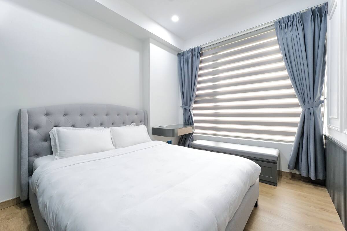 Een moderne hotelkamer met een groot bed, een nachtkastje, een bankje en een raam met zonwering.