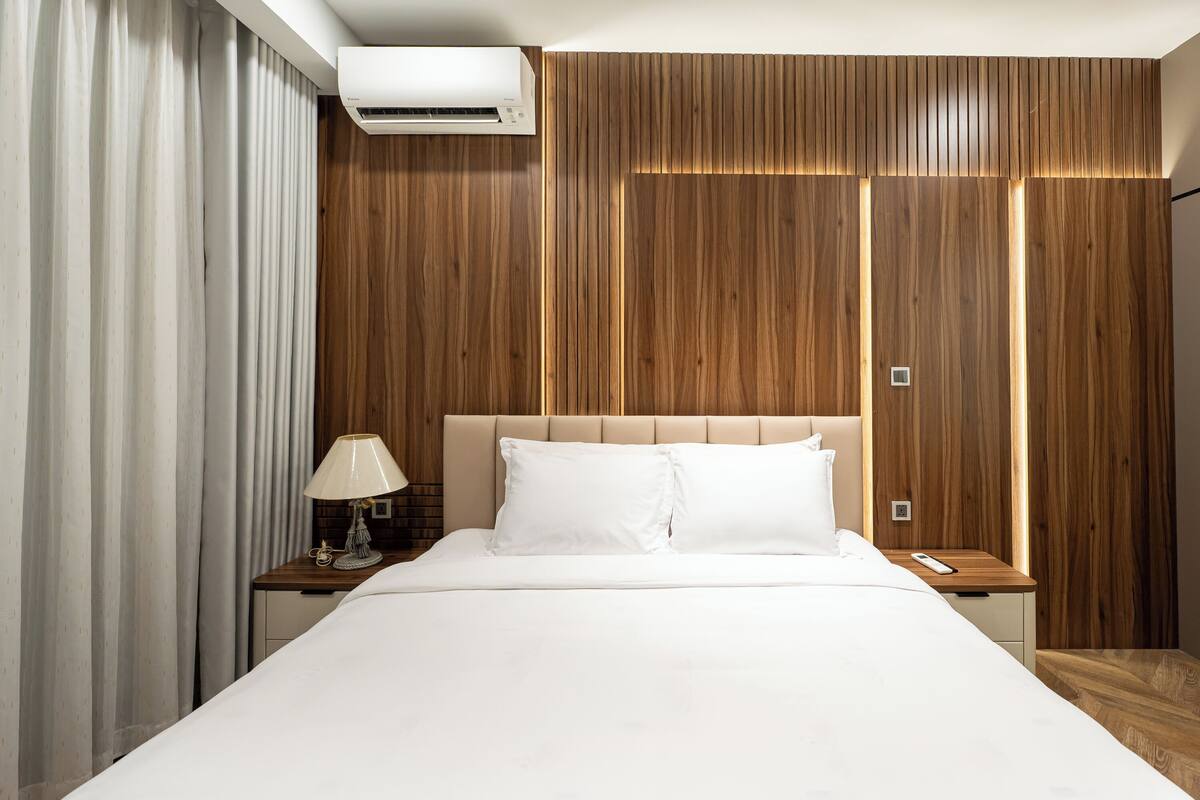Hotelkamer met een groot bed, houten paneelwanden, een nachtkastje met een lamp en een airconditioning.