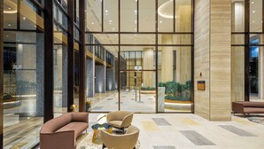 Eine großzügige Lobby mit modernem Design, ausgestattet mit einer Sitzecke mit Sofas und Sesseln, einem Empfangsbereich und Blick auf den Innenhofgarten.