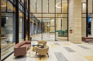 A spacious lobby with a modern design, featuring a seating area with sofas and armchairs, a reception desk, and a view of the indoor garden.