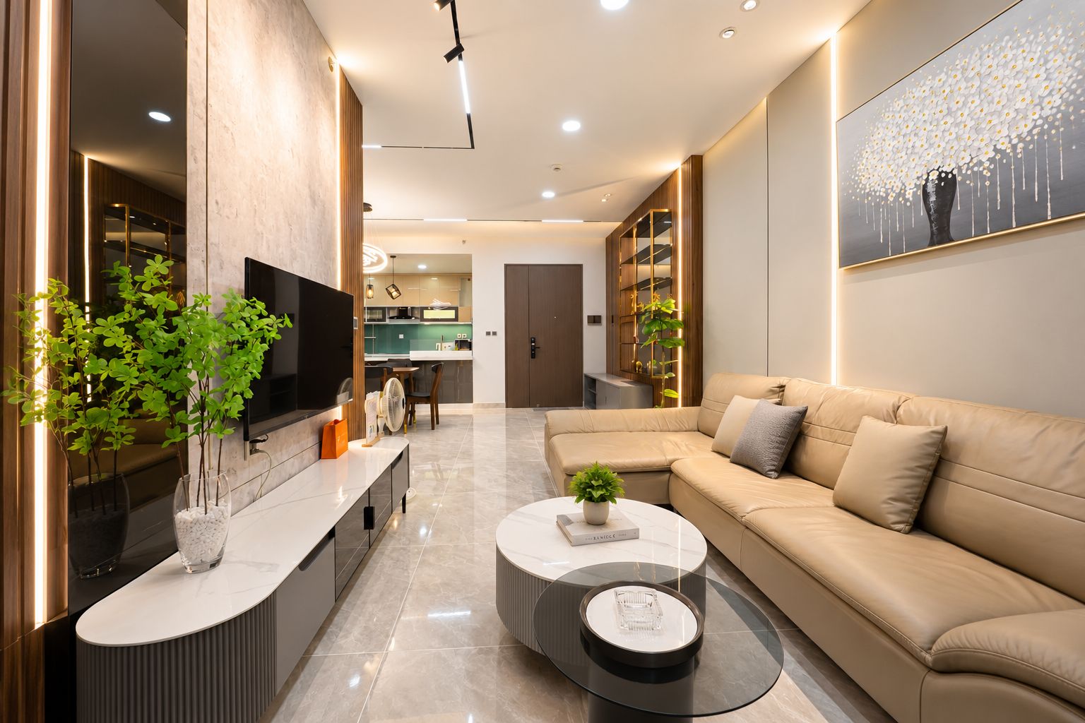 A modern living room with a sofa, coffee table, and TV. There is a kitchen in the background.