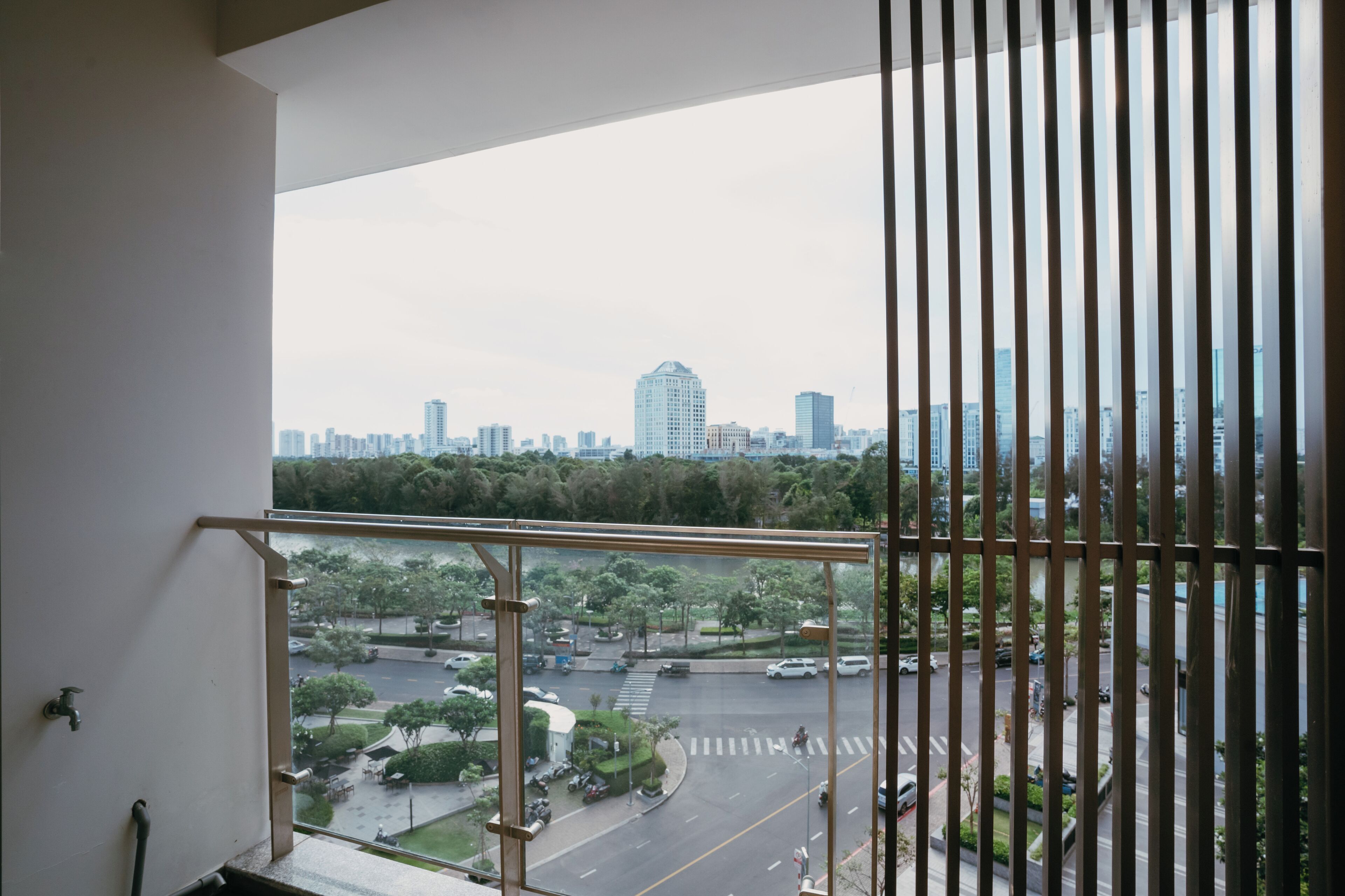 A view from a balcony with a metal railing, overlooking a cityscape with buildings and a road.