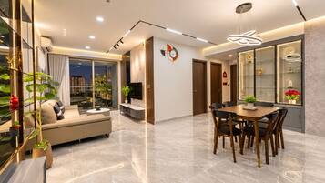 A modern living room with a sofa, coffee table, and TV, a dining area with a table and chairs, and a large window with a city view.