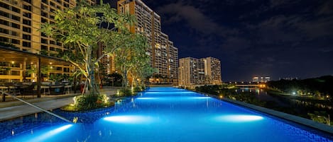 Una piscina nocturna con edificios circundantes y un río.