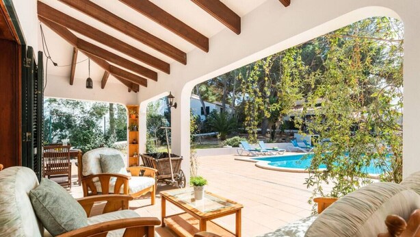 A sunlit patio with wooden furniture, a pool, and a view of trees and a building. - 185 Sud  relax and enjoy Menorca (Son Parc)