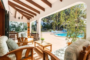 A sunlit patio with wooden furniture, a pool, and a view of trees and a building. - 185 Sud  relax and enjoy Menorca (Son Parc)