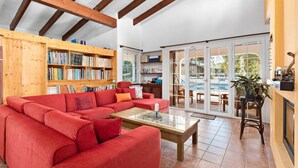 A spacious living room with a red sectional sofa, a wooden bookshelf filled with books, and a glass coffee table. - 185 Sud  relax and enjoy Menorca (Son Parc)