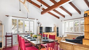 A dining area with a wooden table set for four, surrounded by red chairs. There is a wooden bench with a cushion in the background, and a television on a wooden stand. - 185 Sud  relax and enjoy Menorca (Son Parc)
