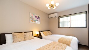 Habitación de hotel con dos camas, una lámpara en el techo, un equipo de aire acondicionado, una ventana con persianas y una obra de arte colgada en la pared.