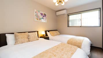 A hotel room with two beds, a ceiling light, an air conditioning unit, a window with blinds, and a wall-mounted artwork.