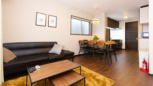 Una sala de estar moderna con un sofá de cuero negro, una mesa de centro de madera y un comedor con mesa y sillas.