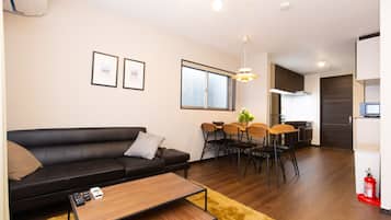 A modern living room with a black leather sofa, a wooden coffee table, and a dining area with a table and chairs.