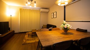 Una sala de estar moderna con una mesa de comedor de madera, asientos cómodos, un televisor de pantalla plana y una lámpara en el techo.