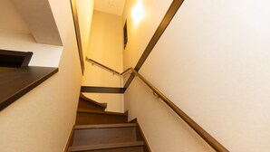 Una escalera de madera con barandales de metal, que conduce a un rellano con una lámpara.