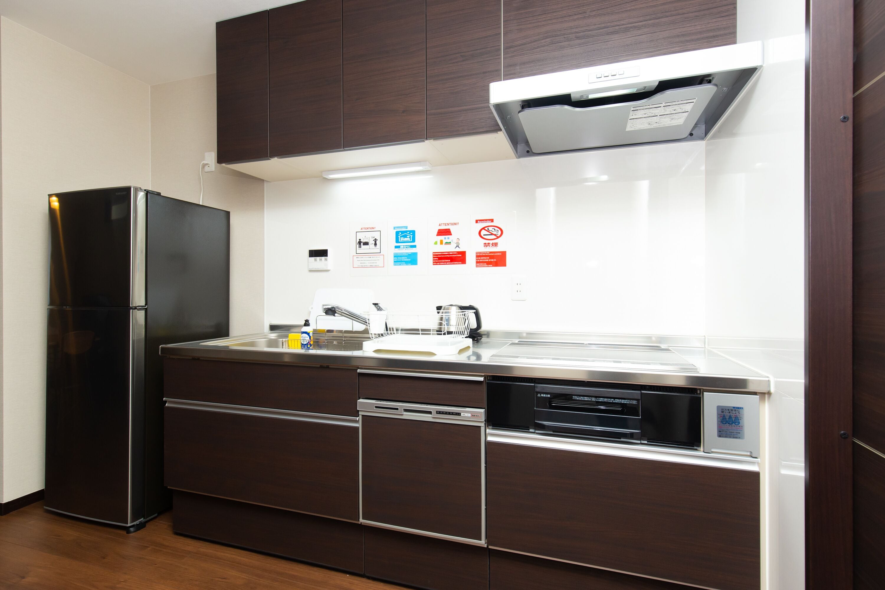 A modern kitchen with a built-in refrigerator, dishwasher, and oven. There are several safety signs on the wall.