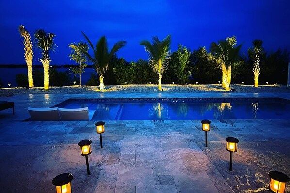 A swimming pool area at night with palm trees and illuminated lanterns.