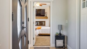 A hallway leading to a bedroom with a bed, a nightstand, a lamp, and a ceiling fan.