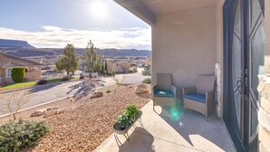 A balcony with a view of a residential area, a wicker chair, and a small table with a plant.