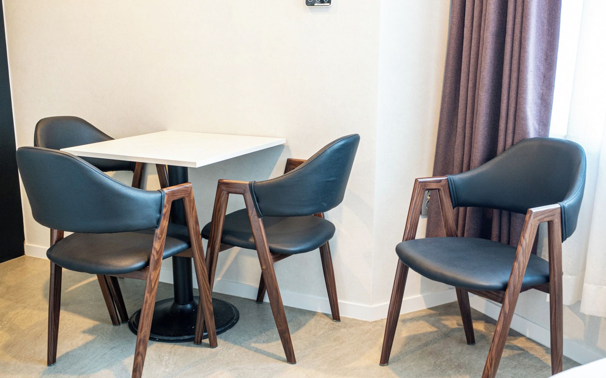 Una habitación con una mesa blanca y cuatro sillas con estructura de madera y asientos negros.