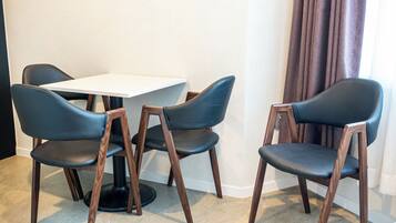 Una habitación con una mesa blanca y cuatro sillas con estructura de madera y asientos negros.