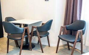 A room with a white table and four chairs with wooden frames and black seats. - CS Avenue Hotel (Seoul)