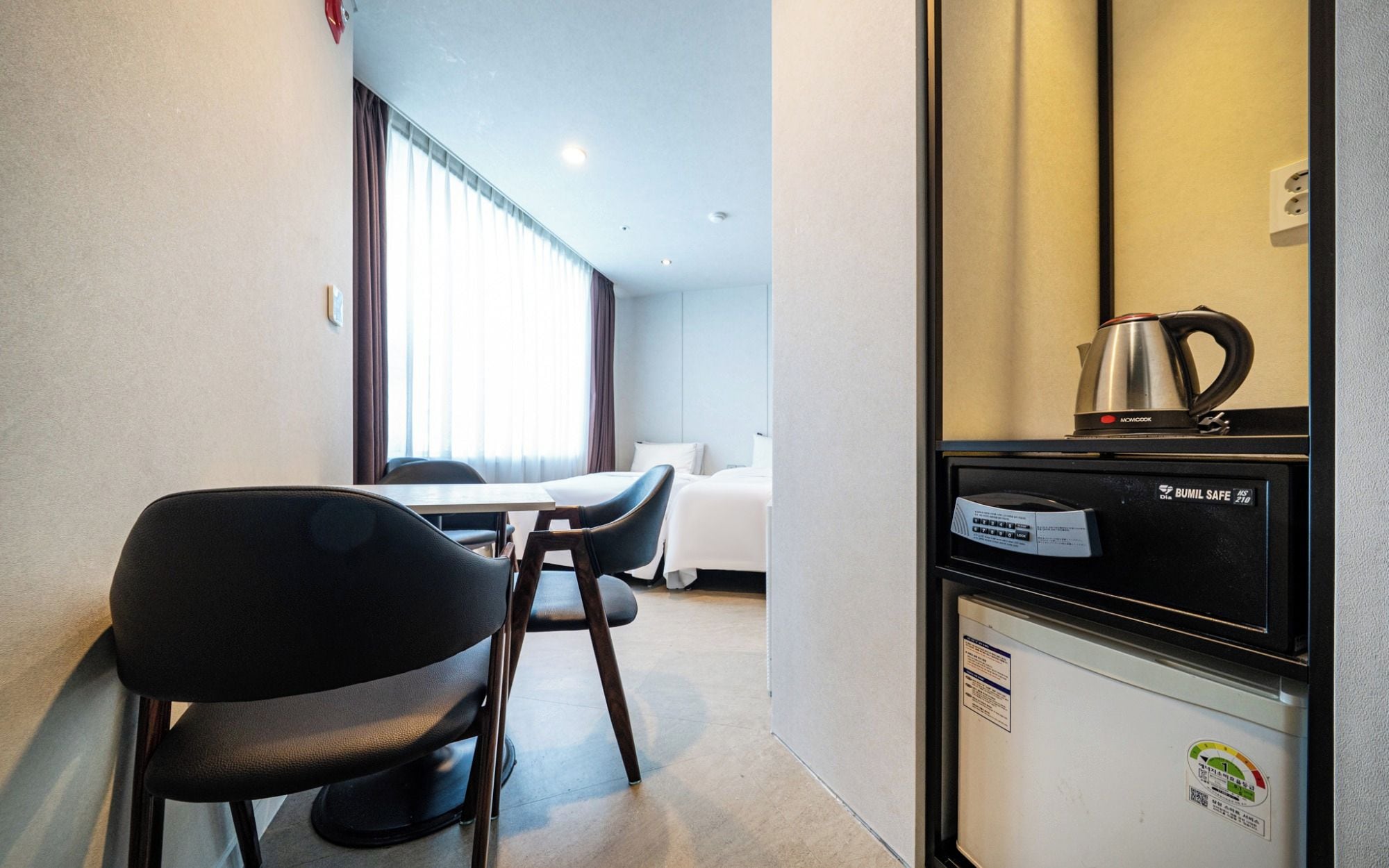 A hotel room with a kitchenette, a dining area with a table and chairs, and a bed with white bedding.
