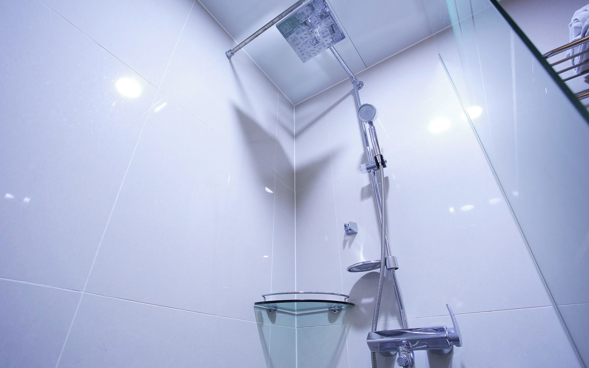 A modern bathroom with white tiles, a glass shower enclosure, and a glass sink.