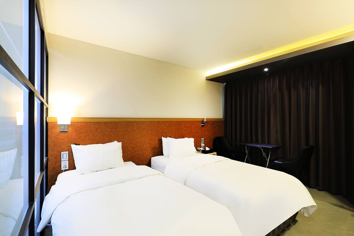 Habitación de hotel con dos camas, un escritorio, una silla y una cortina.