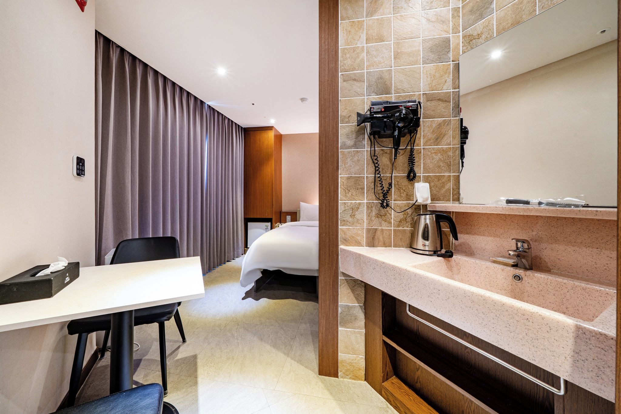 Ein Hotelzimmer mit einem Bett, einem Schreibtisch mit Stuhl, einem Telefon und einem Badezimmer mit Waschbecken und Spiegel.