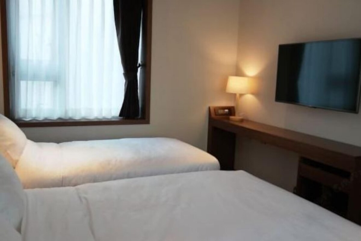 Habitación de hotel con dos camas, un televisor en la pared y una ventana con cortinas.