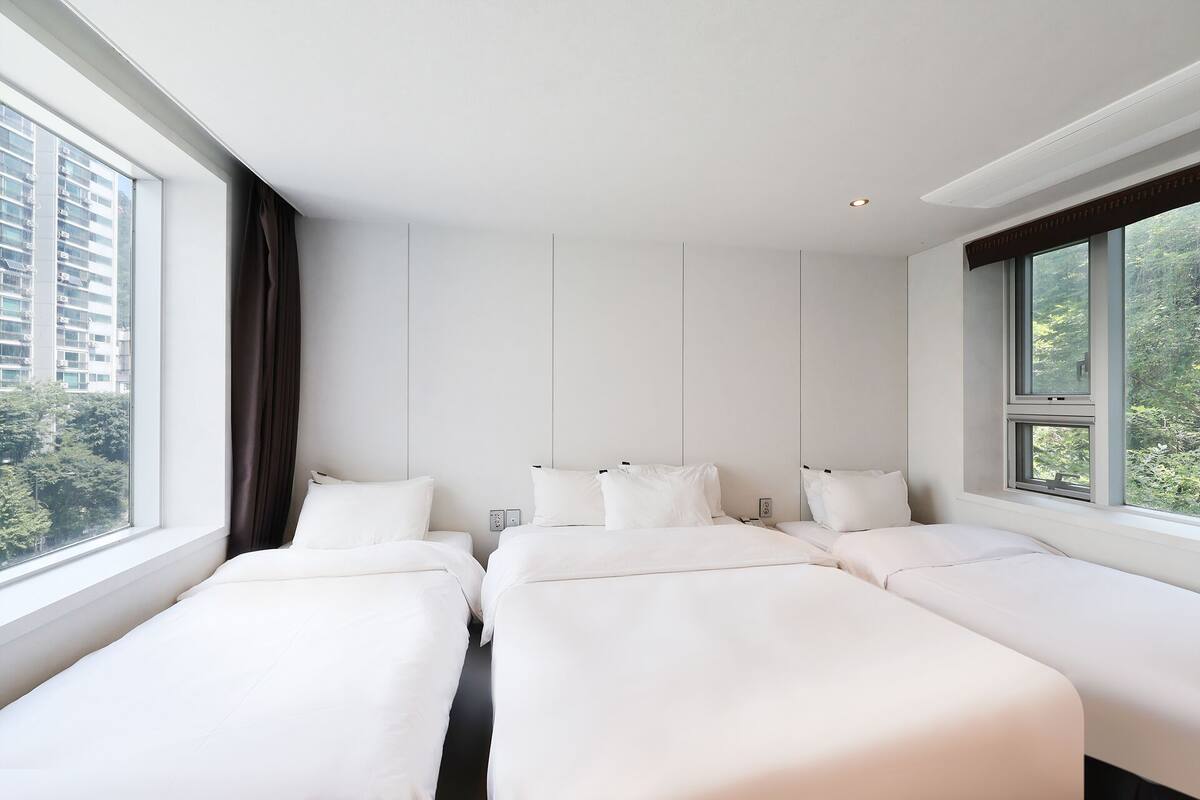 Una habitación de hotel con dos camas, un ventanal grande y vistas a edificios y árboles.