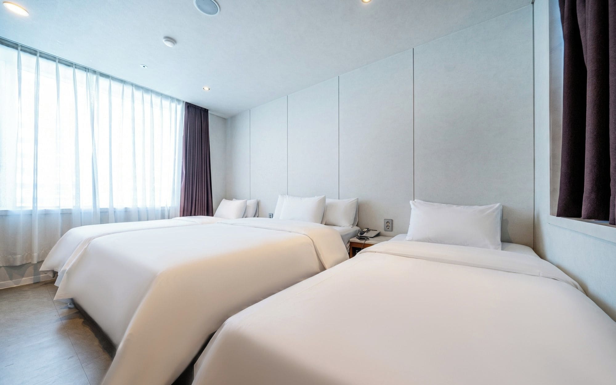 Habitación de hotel con dos camas, un ventanal grande con cortinas y un diseño moderno.
