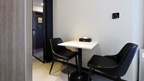 Ein kleines Zimmer mit einem weißen Tisch und zwei schwarzen Stühlen, einer Taschentuchbox auf dem Tisch und einer Tür zu einem anderen Raum.