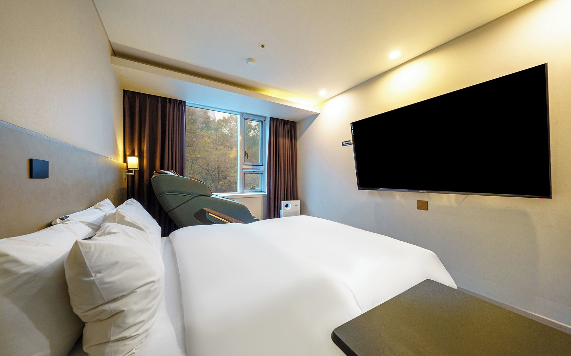 Quarto de hotel com cama, cadeira, televisão de tela plana e janela com cortinas.