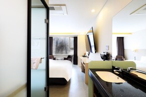Enjoy a spacious room with a large bed, separate desk area, and bathroom featuring a large mirror and sink, offering a city view.