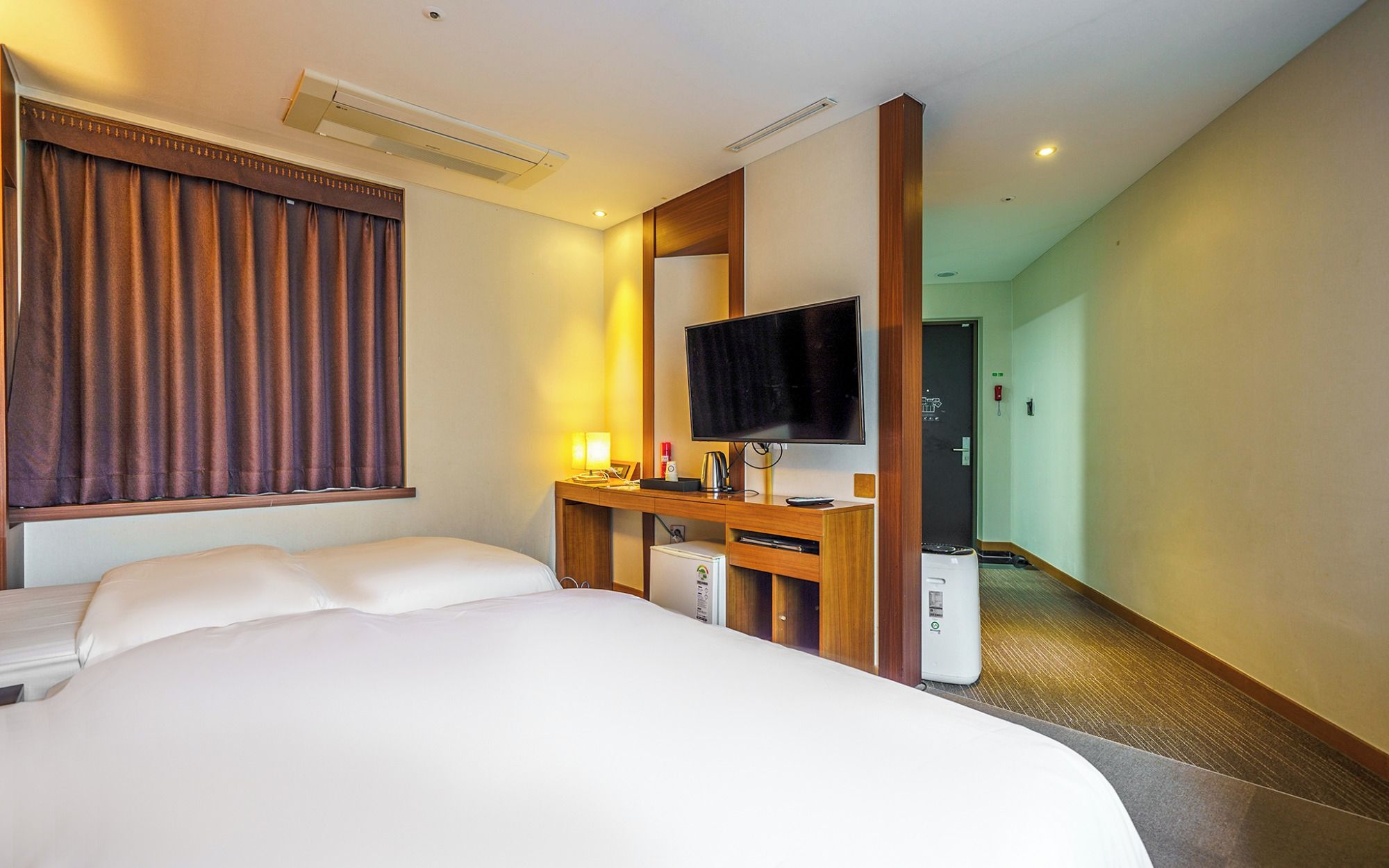 A hotel room with a bed, a desk with a television, and a small kitchenette.