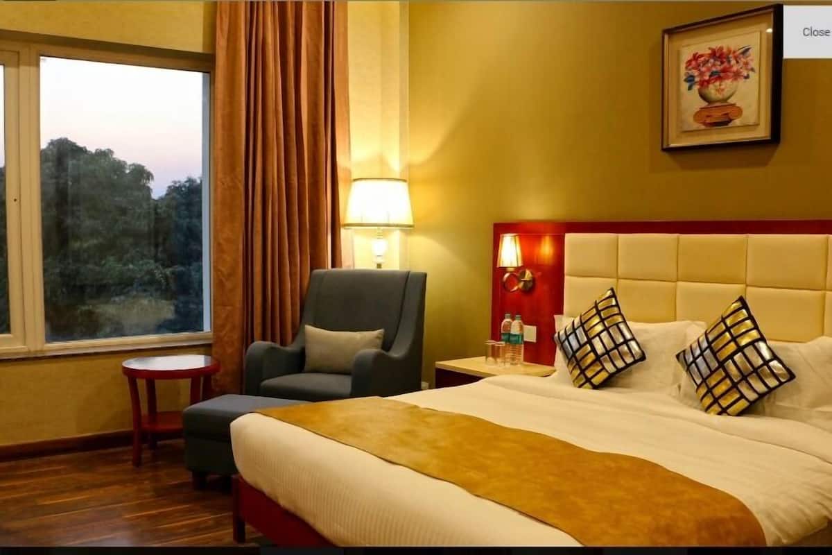 A hotel room with a large bed, a chair, a small table, a lamp, and a painting on the wall.