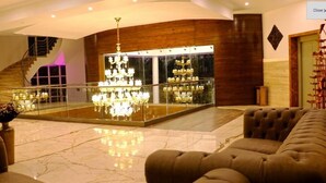 A spacious lobby with a grand chandelier, a staircase, and a glass display case with shoes. - Tiaraa Hotels & Resorts (Ramnagar)