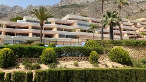 Un hotel de varios pisos con balcones, palmeras y montañas al fondo.