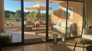 Amplia sala de estar con puerta corrediza de vidrio que da a un patio exterior. El patio cuenta con un sofá, una mesa de centro y una sombrilla.