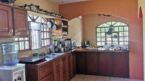 A kitchen with wooden cabinets, a water dispenser, a sink, and a window with a view of greenery.