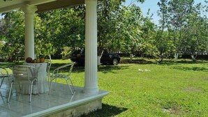 A covered patio with a table and chairs, surrounded by a grassy lawn and trees.
