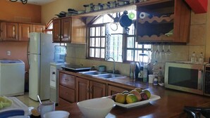 A kitchen with wooden cabinets, a refrigerator, a microwave, and a sink. There are fruits on the counter and a window with curtains.