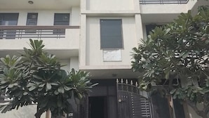 A multi-story residential building with a central entrance, balconies, and surrounding greenery. - CWR Stays (Noida)