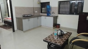 A compact kitchen with a dining area, a water dispenser, and a kettle on the table. - CWR Stays (Noida)