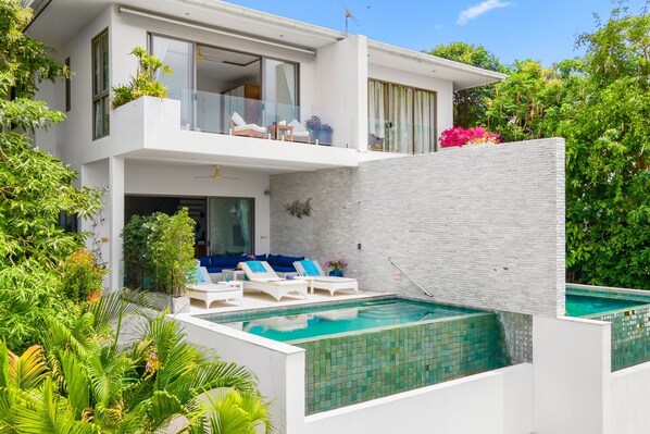 Uma casa moderna de dois andares com piscina, área de estar externa e vegetação exuberante.