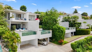 Um edifício residencial moderno com piscina no terraço, área de estar coberta ao ar livre e um carro na entrada.