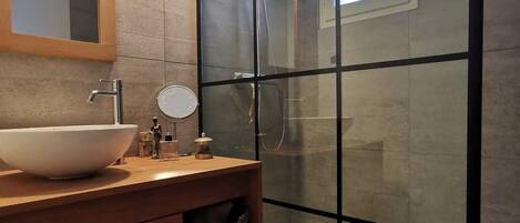 Un baño moderno con ducha envuelta en vidrio, tocador de madera con un lavabo grande y un espejo sobre el tocador.