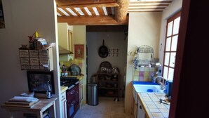 Una cocina estrecha con vigas de madera, suelo de baldosas y electrodomésticos sencillos.